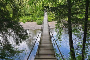 Fototapeta premium Suspension bridge across the river. River Serga, Natural Park Deer Streams, Sverdlovsk oblast, Russia.