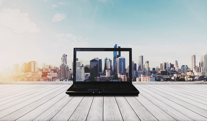 Computer laptop on white wood floor with Bangkok city view in sunrise background