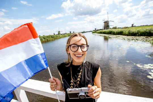 Young woman tourist standing with dutch flag on the beautiful landscape backgorund with old windmills in Netherlands