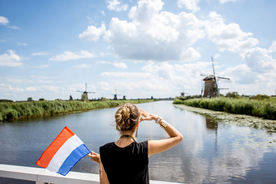 Young woman tourist standing back with dutch flag enjoying great view on the beautiful landscape with old windmills in Netherlands