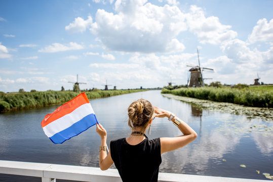 Young woman tourist standing back with dutch flag enjoying great view on the beautiful landscape with old windmills in Netherlands