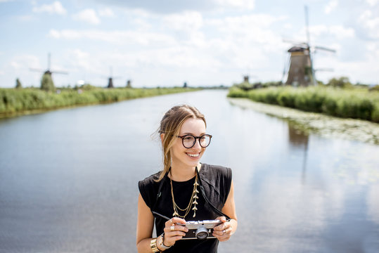 Portrait of a young woman tourist standing with photo camera on the beautiful landscape background with old windmills in Netherlands
