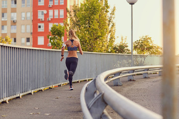 Sporty girl runner runs on a bridge in the city in autumn summer.