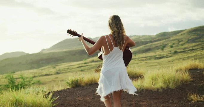 Happy young woman playing guitar at sunset