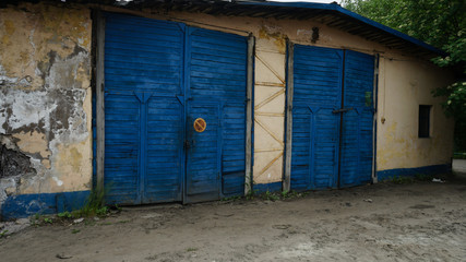 Obraz na płótnie Canvas Two big wood blue garage gates in small building. Walls of house are lost their origin colors.