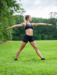 Young fit female in workout clothes stretching in the park.