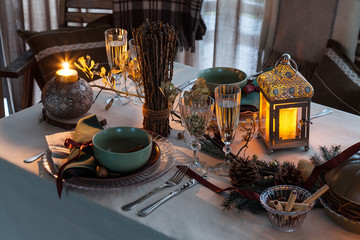 Fototapeta na wymiar Cozy festive table with burning candles, wineglasses and plates. Romantic dinner for two persons. Large platter with main dish, champagne in glasses. Plaid on the back of a chair. View from above.