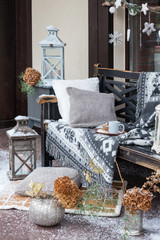 Vintage blanket on wooden bench with pillows, candlesticks, cup of coffee. Rustic style. Cozy plaid lie on snowed chair. New year decorations. Winter Christmas background.