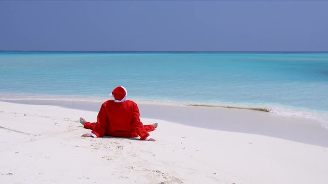 Man in Santa Claus Hat sitting on sandy beach. Christmas vacation on Maldivian islands