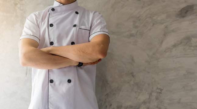 Handsome caucasian man professional Chef arms crossed in white uniform on gray cement wall with copyspace