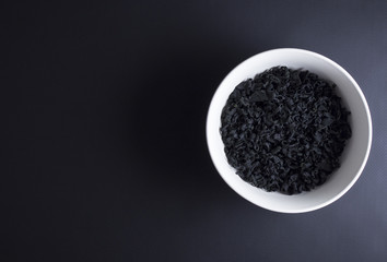 Dried wakame seaweed in white and grey bowl isolated on black background
