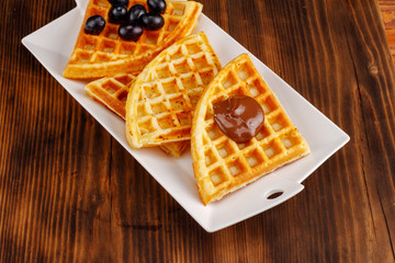 Waffles with honey, jam, and berries on a white plate, on wooden background