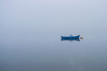 Boat on calm late water in a foggy morning