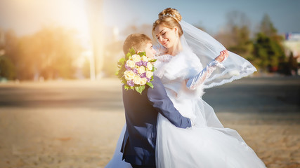 The bride and groom are hugging in the sun.