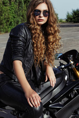 Fototapeta na wymiar young woman in leather clothes and sunglasses near a motorcycle