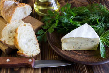 Cheese with herbs and baguette on the wooden background