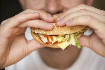 Man eating hamburger with vegetables at a fast food restaurant, fast food knowns like unhealthy...