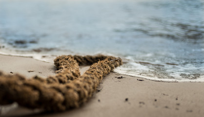 A rope is laying in the sand on a beach doing its best to keep the waves of water at bay