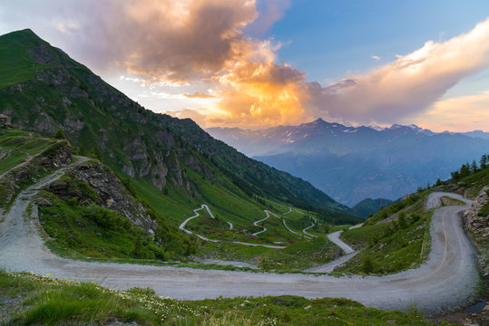 Dirt mountain road leading to high mountain pass in Italy (Colle delle Finestre). Expasive view at sunset, colorful dramatic sky, adventures in summer time, Italian Alps.