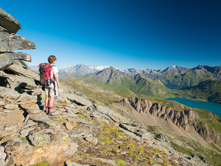 Naklejka na ściany i meble Woman trekking in high altitude rocky mountain landscape. Summer adventures on the Italian French Alps