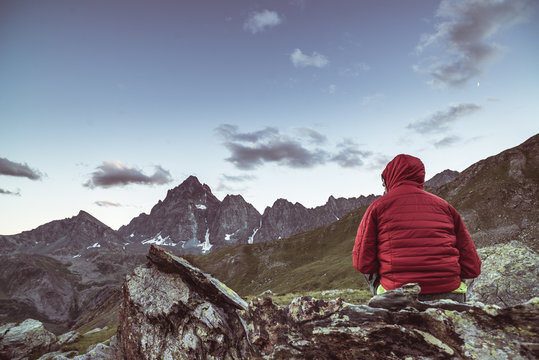 One Person Sitting On Rocky Terrain And Watching A Colorful Sunrise High Up In The Alps. Wide Angle View From Above With Glowing Mountain Peaks In The Background. Toned Image.