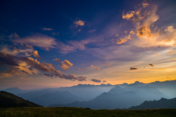 Colorful sunlight on the majestic mountain peaks, green pastures and foggy valleys of the Italian Alps. Golden cloudscape at sunset.
