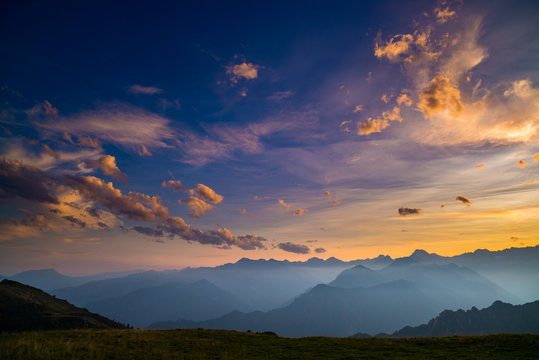 Colorful Sunlight On The Majestic Mountain Peaks, Green Pastures And Foggy Valleys Of The Italian Alps. Golden Cloudscape At Sunset.