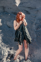 Rothaarige Frau , mittleren Alters bedeckt Ihren nackten Körper mit einer alten Lederjacke, stehend im tiefen Sand