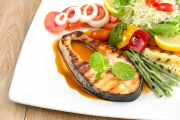Salmon grill on teriyaki sauce and vegetable grill in white dish on the wooden table
