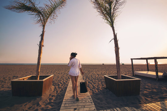 Woman calling by phone and walking on beach.Back view image of young woman standing at beach and talking by her phone