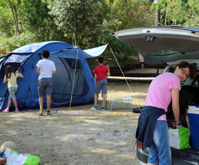 Mom loads the car while the kids mount the tent in the campsite