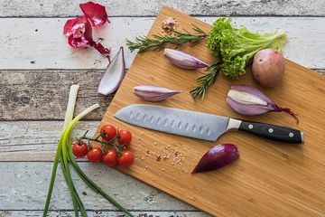 Knife with healthy food - vegetables, onion, salad, tomatoes, potato placed on a cutting board with wood background top view