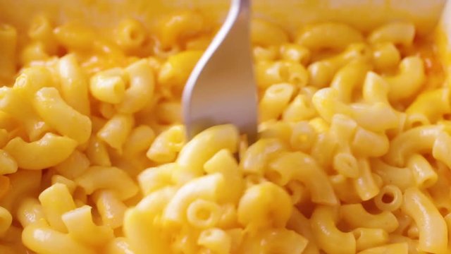 Close video of macaroni and cheese in a microwavable paper tray being slowly stirred with a fork after heating..