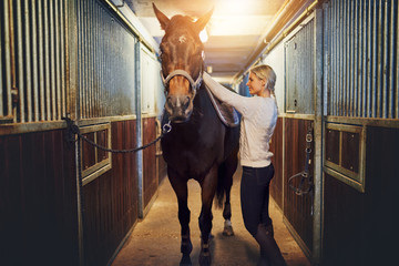 Woman standing with her horse in stables before a ride