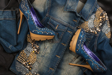 Shoes and jacket from denim fabric inlaid rhinestones lying on a black silk.