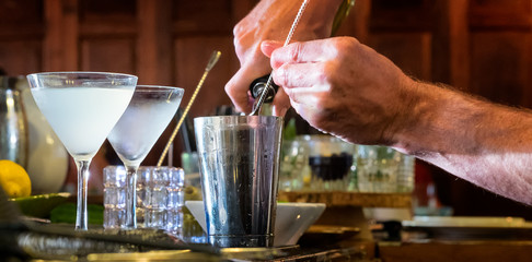 Bartender mixes a cocktail. Close up in a bar setting. Chilled frosty glasses.