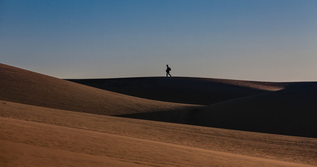 Shadow of a tourist walking on the shadowed sand dunes 