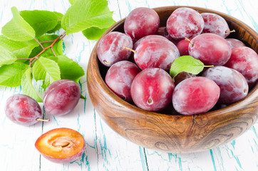 Plums in wooden bowl with green leaves on the table