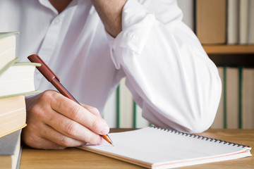 Man's hand with pen writing something in the notebook on the table. Education concept.