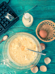 Making waffles at home - waffle iron, batter in bowl and ingredients - milk, eggs and flour.