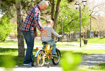 Cute little boy riding on bicycle and his grandfather in spring park