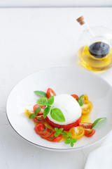 Delicious caprese salad with ripe cherry tomatoes and mozzarella cheese with fresh basil leaves and olive oil. Italian healthy food concept with copy space