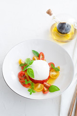 Delicious caprese salad with ripe cherry tomatoes and mozzarella cheese with fresh basil leaves and olive oil. Italian healthy food concept with copy space