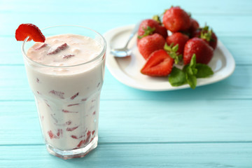 Delicious milk cocktail and plate with sliced strawberry on wooden table