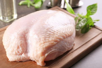 Cutting board with fresh raw turkey fillet and basil leaves on table