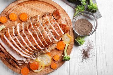 Cutting board with delicious sliced turkey fillet and vegetables on table