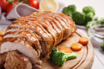 Cutting board with delicious sliced turkey fillet and vegetables on table