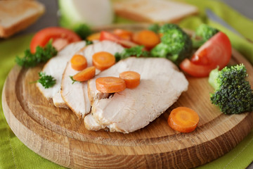 Cutting board with delicious sliced turkey fillet and vegetables on table, closeup