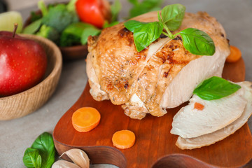 Cutting board with delicious sliced turkey fillet and vegetables on table