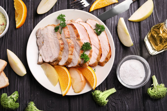 Plate with delicious sliced turkey fillet and fruits on wooden table